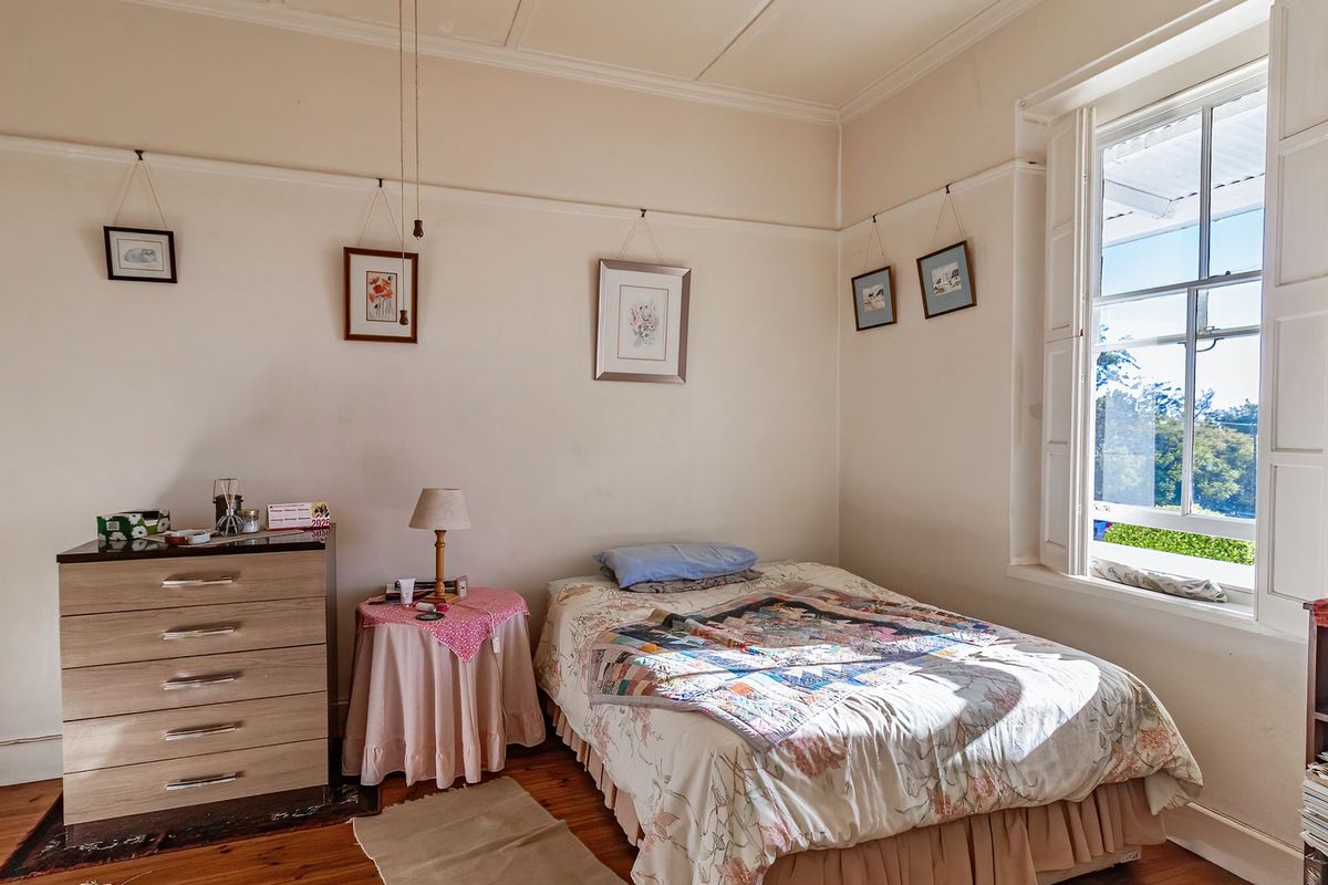 A cozy bedroom featuring original timber flooring, a classic sash window with shutters, and traditional picture rails.