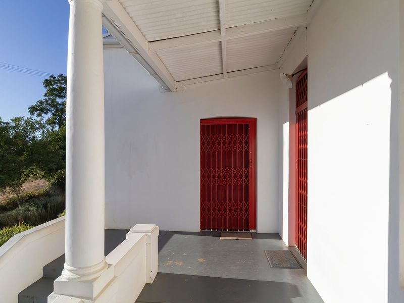 A covered patio area featuring a classical column, concrete flooring, and red security gates providing access to the home.