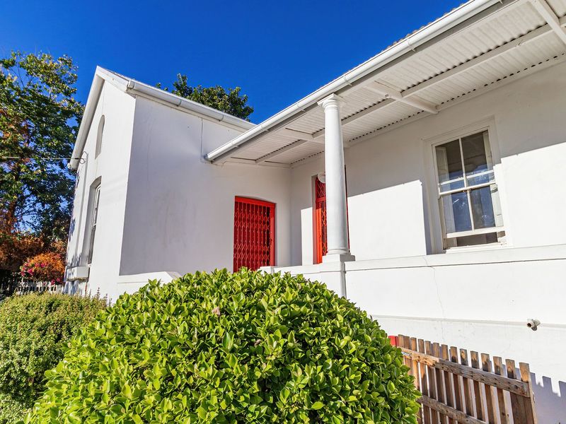 Front elevation of a classic home featuring a covered veranda with a decorative column, red security gate, and white painted masonry walls.