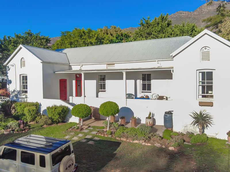 A charming single-story residence featuring a classic corrugated metal roof, a covered front veranda, and established garden surroundings with mountain views.
