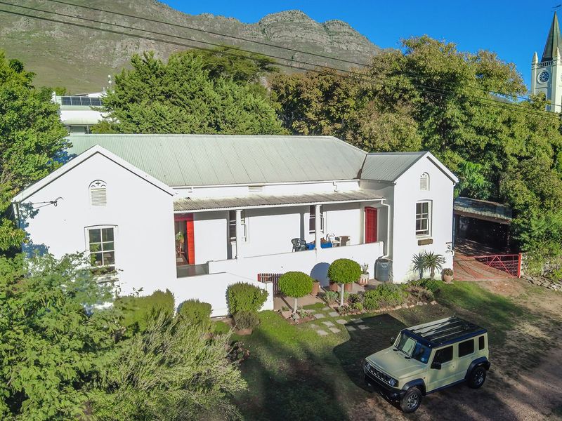 A charming single-story residence featuring a metal roof, covered veranda, and classic sash windows, set against a scenic mountain backdrop.