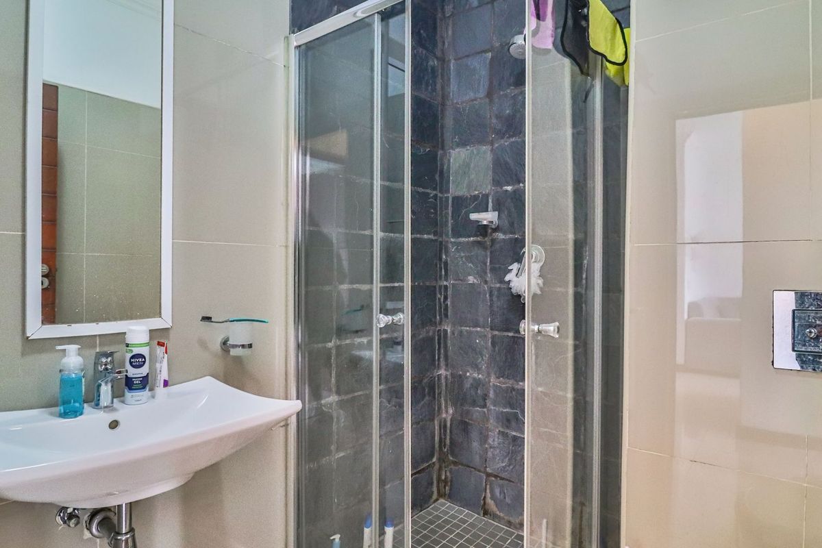 A functional bathroom featuring a wall-mounted basin, a framed mirror, and a glass-enclosed shower with dark stone-look wall tiles.