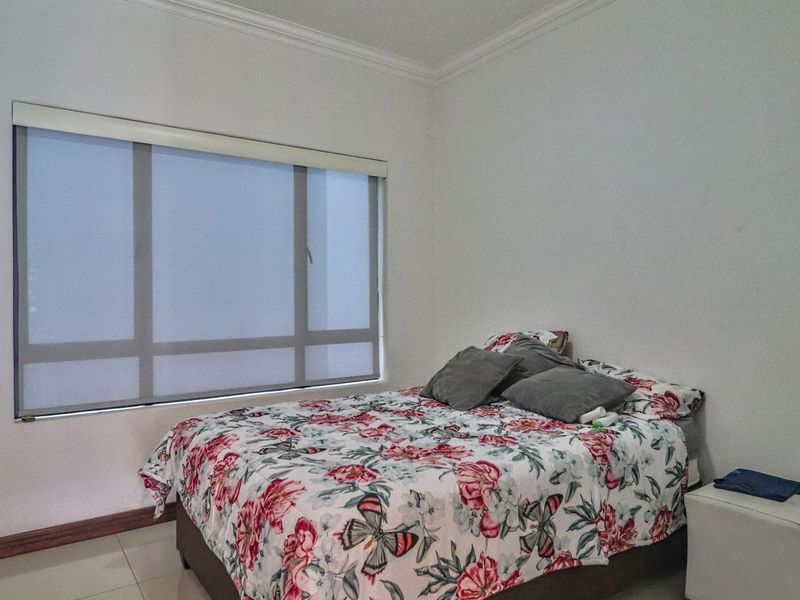 A bedroom featuring tiled flooring, crown molding, and a large window with a fitted roller blind.