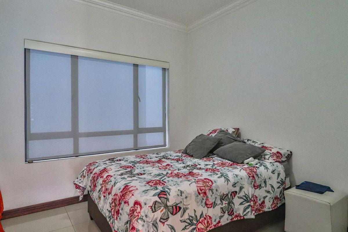 A bedroom featuring tiled flooring, crown molding, and a large window with a fitted roller blind.