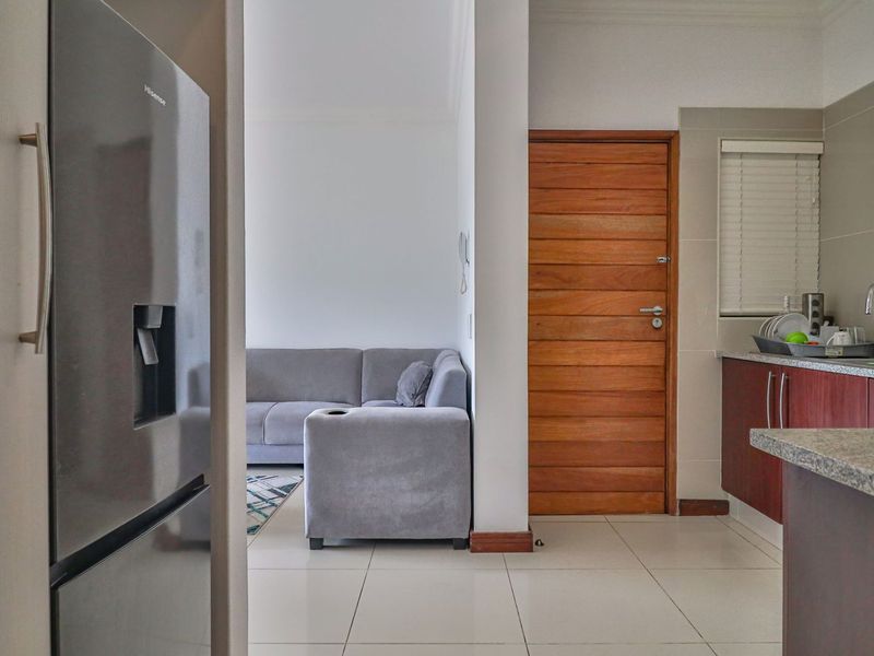 A view from the kitchen looking into the living area, featuring tiled flooring, wooden cabinetry, and a solid timber door.