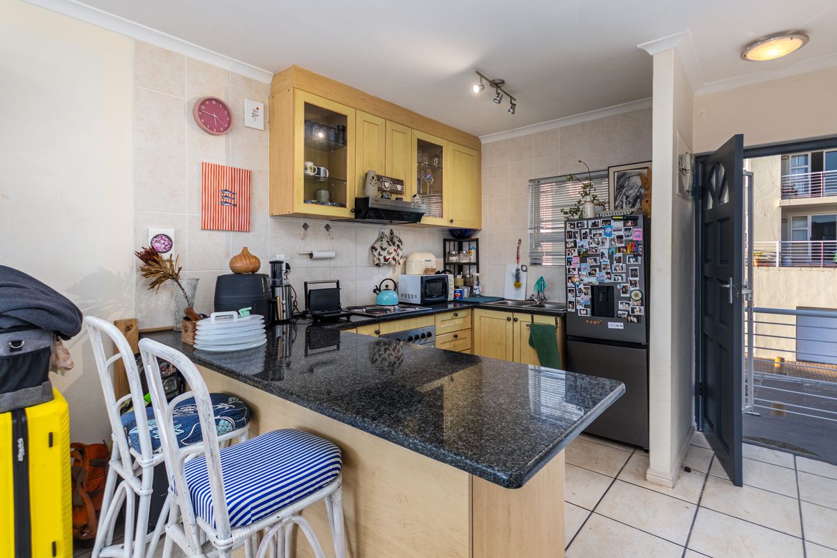 Compact kitchen featuring light wood cabinetry, dark granite countertops, a breakfast bar, and tiled flooring, with direct access to an outdoor balcony.