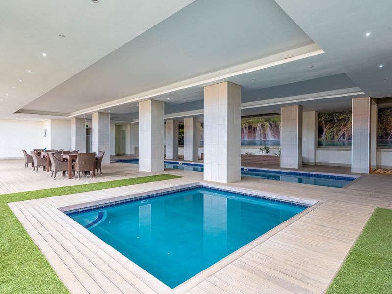 A spacious indoor pool area featuring tiled decking, recessed ceiling lighting, and structural columns, providing a modern communal leisure space.