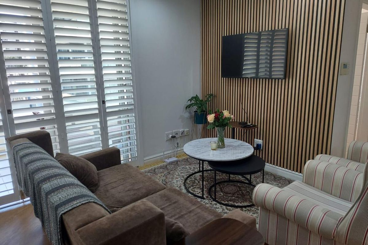 A cozy living room featuring a decorative timber slat feature wall, white plantation shutters, and wood-look flooring.