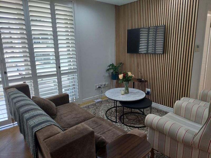 A cozy living room featuring a decorative timber slat feature wall, white plantation shutters, and wood-look flooring.