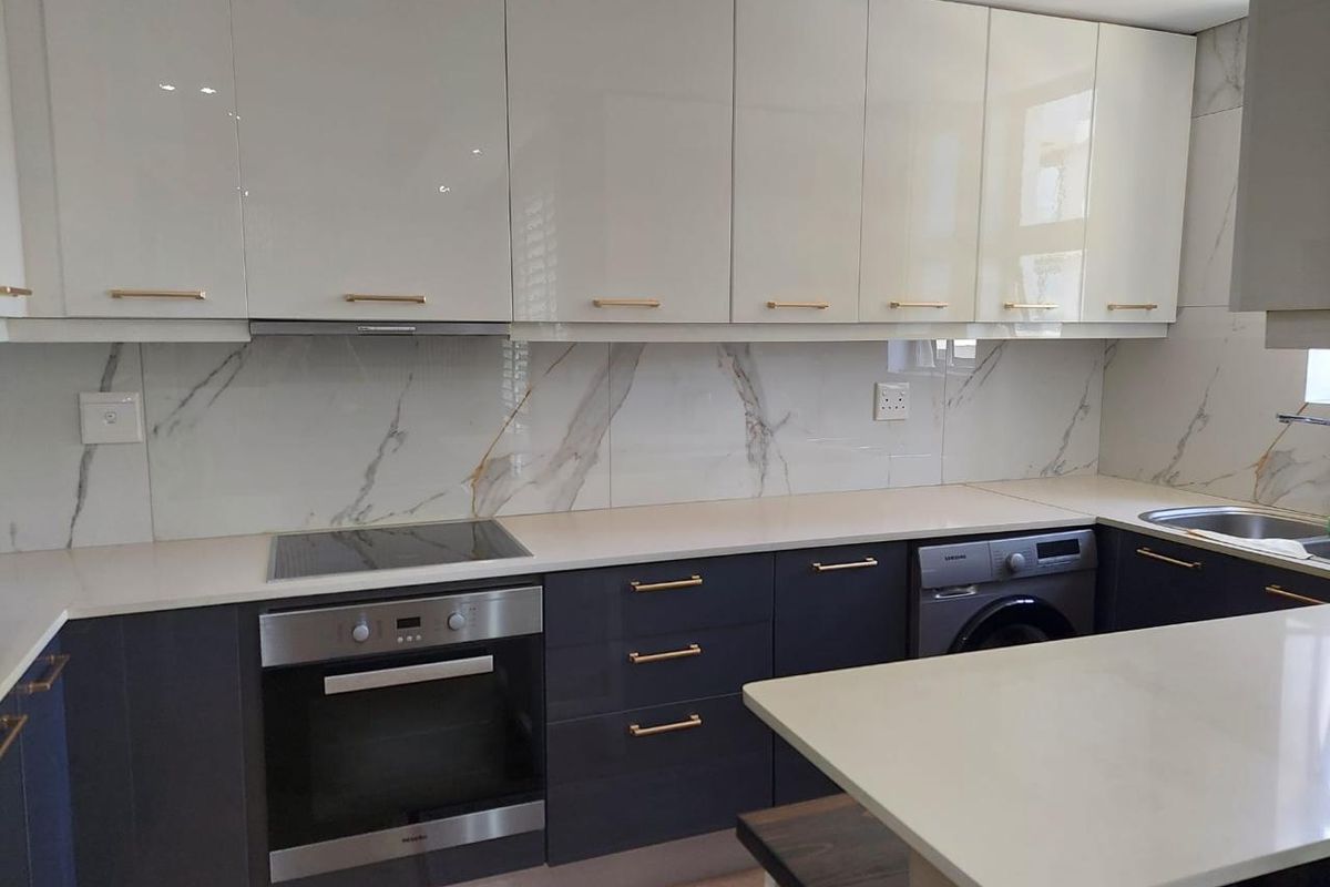 Modern kitchen featuring high-gloss cabinetry, marble-look splashback, stone countertops, integrated oven, induction hob, and built-in laundry appliance.