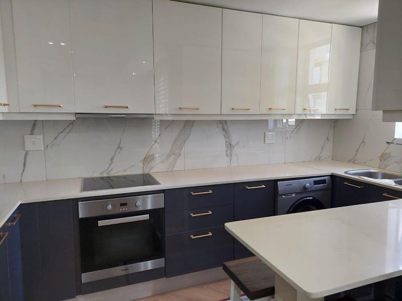 Modern kitchen featuring high-gloss cabinetry, marble-look splashback, stone countertops, integrated oven, induction hob, and built-in laundry appliance.