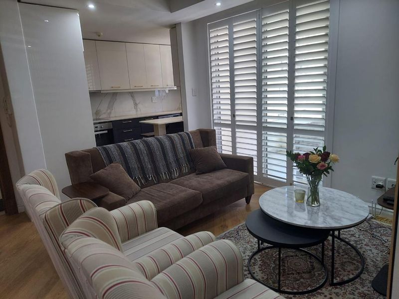 Open-plan living area featuring modern kitchen cabinetry, integrated appliances, and large windows with fitted plantation shutters, creating a bright and functional space.