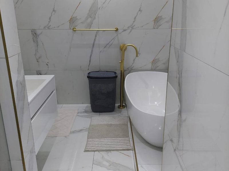 Modern bathroom featuring a freestanding bathtub with gold floor-mounted faucet, marble-look wall and floor tiles, and a sleek wall-mounted vanity.
