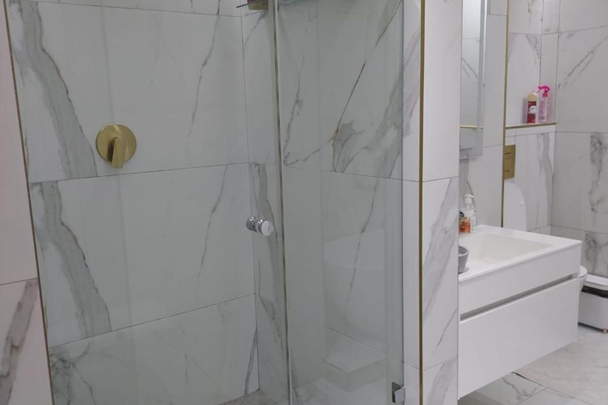 Modern bathroom featuring a glass-enclosed walk-in shower with gold-toned fixtures, marble-look wall tiles, and a sleek wall-mounted vanity unit.