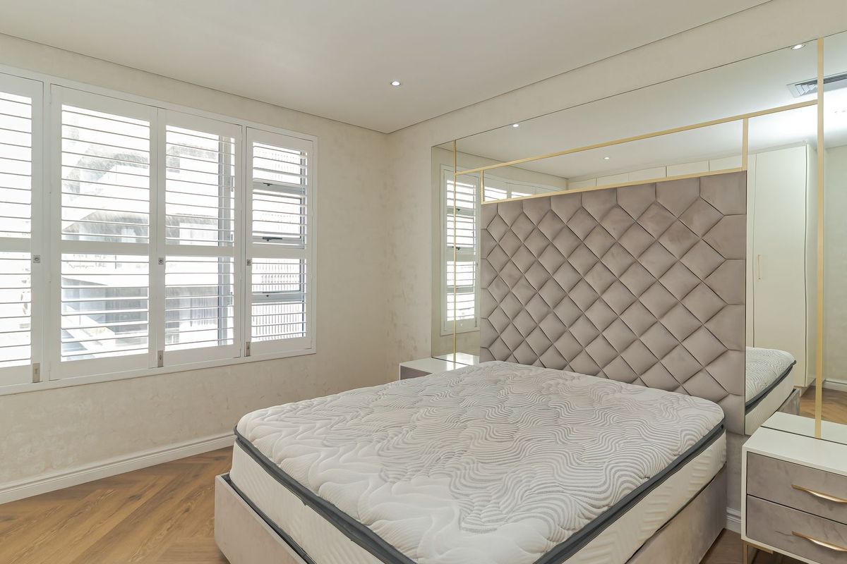 A well-appointed bedroom featuring timber flooring, plantation shutters, recessed lighting, and a large mirrored feature wall with integrated wardrobe space.