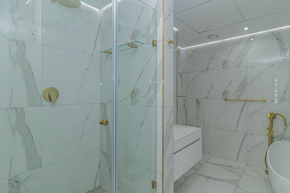 Modern luxury bathroom featuring marble-look tiling, a walk-in shower with glass enclosure, a freestanding bathtub, and elegant brass hardware.