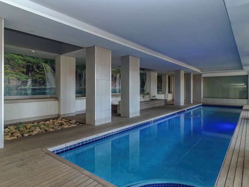 A modern indoor swimming pool area featuring timber decking, structural tiled columns, and decorative wall murals with recessed ambient lighting.