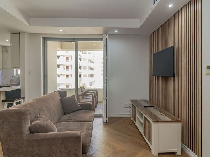 Modern open-plan living area featuring herringbone timber flooring, a stylish slatted wood feature wall, and a seamless transition to the balcony.