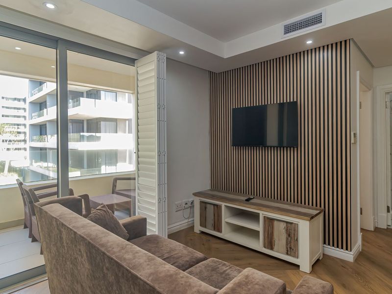 Modern living room featuring stylish slatted timber wall paneling, herringbone flooring, recessed lighting, and seamless access to a private balcony through sliding glass doors.