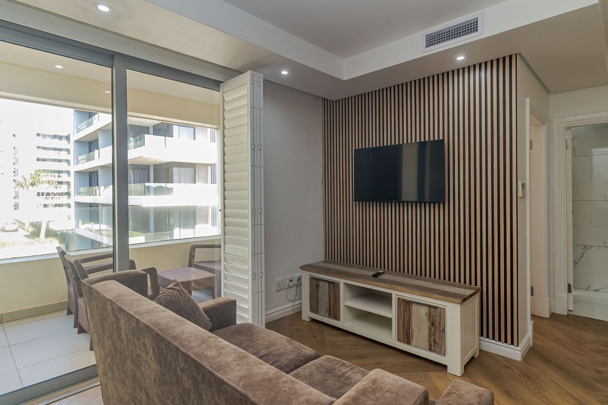 Modern living room featuring stylish slatted timber wall paneling, herringbone flooring, recessed lighting, and seamless access to a private balcony through sliding glass doors.