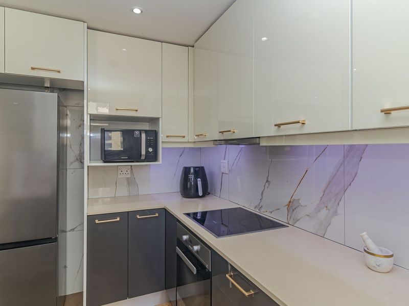 Modern kitchen featuring high-gloss cabinetry, stone countertops, marble-look splashback, and integrated appliances including an oven and electric cooktop.