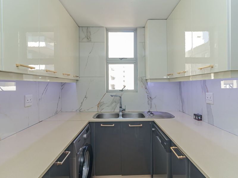 Modern galley-style kitchen featuring high-gloss cabinetry, marble-look splashbacks, stone countertops, and integrated sink with contemporary gold-tone hardware.