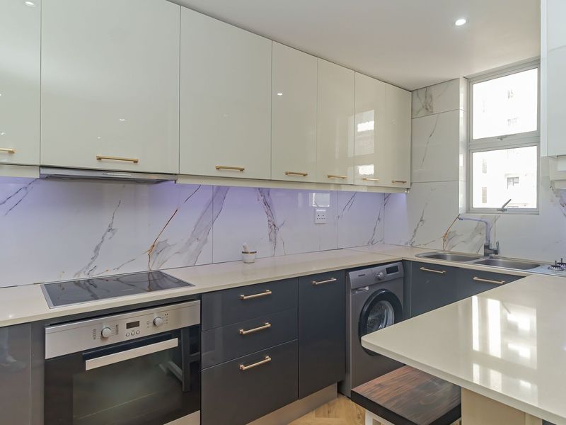 Modern kitchen featuring high-gloss cabinetry, quartz countertops, marble-look splashbacks, integrated appliances, and sleek gold-tone hardware.