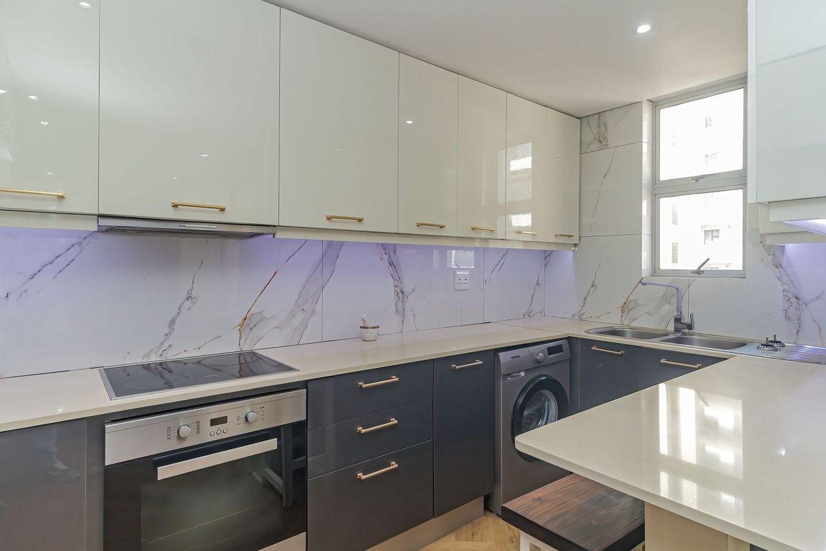 Modern kitchen featuring high-gloss cabinetry, quartz countertops, marble-look splashbacks, integrated appliances, and sleek gold-tone hardware.