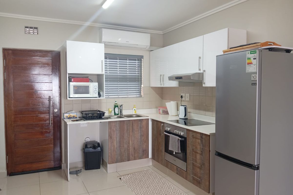 A compact kitchen featuring modern two-tone cabinetry, a built-in oven with hob, extractor fan, stainless steel sink, and a wall-mounted air conditioning unit.