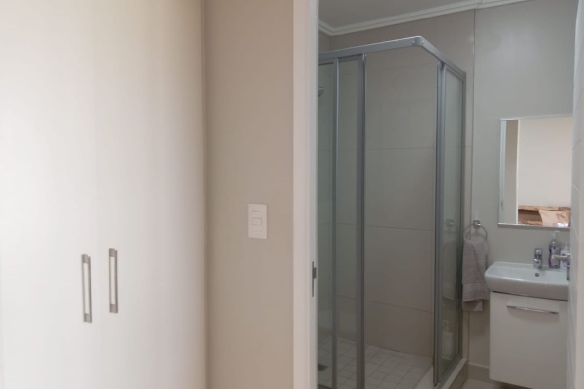 A compact bathroom featuring a glass-enclosed shower, a wall-mounted vanity with a basin, and adjacent built-in cupboards.
