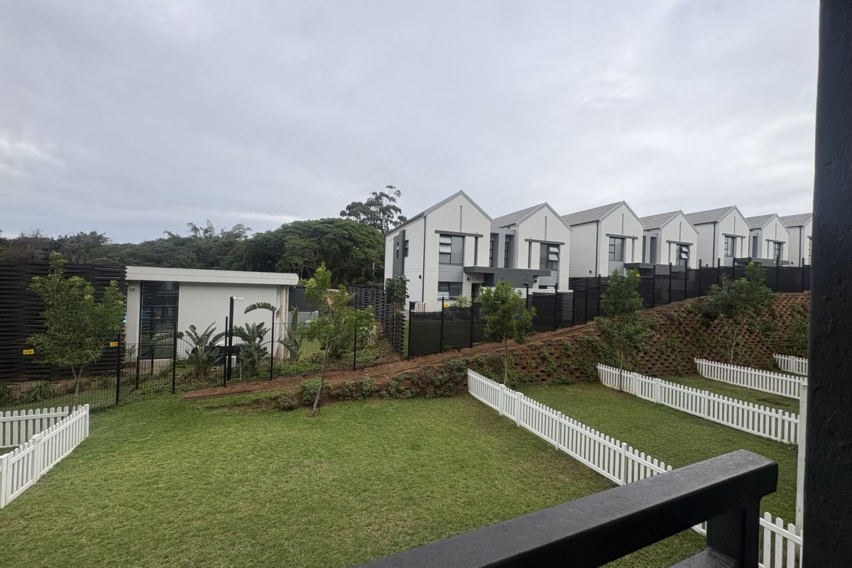A view of the residential complex featuring modern townhouses, landscaped garden areas with white picket fencing, and a well-maintained communal outdoor space.