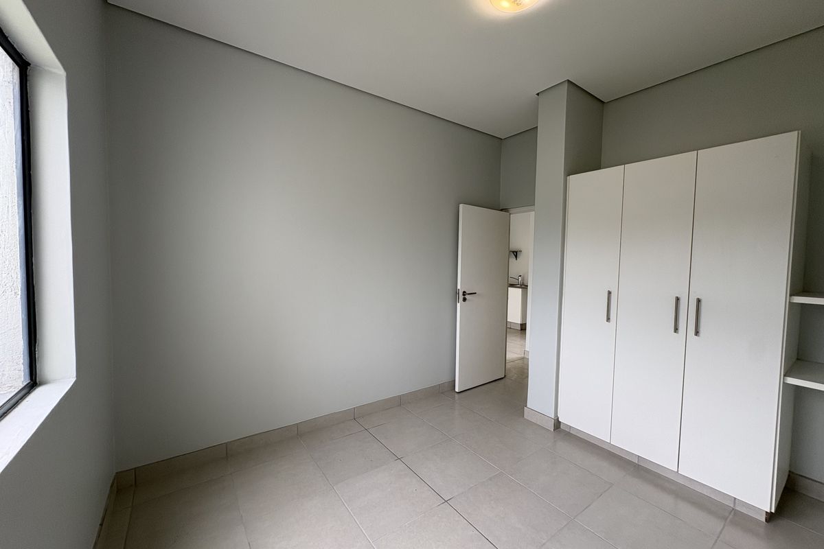 A clean, empty bedroom featuring neutral tiled flooring, a built-in white wardrobe, and a simple ceiling light fixture.