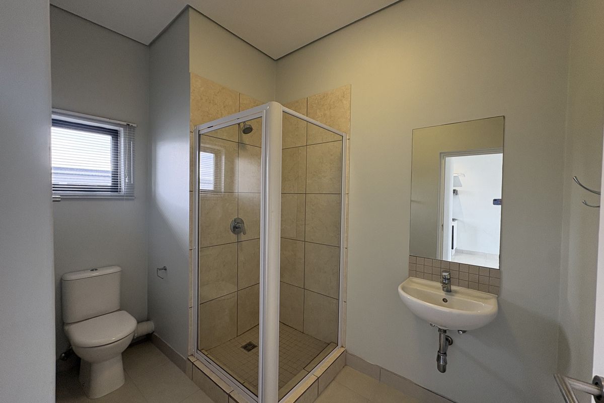 A clean and functional bathroom featuring a corner shower enclosure, wall-mounted basin, and toilet with neutral tiling.