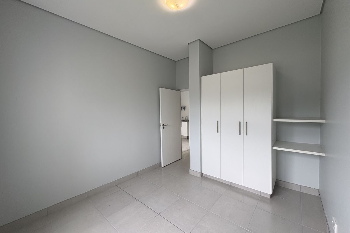 A clean, empty bedroom featuring neutral tiled flooring, built-in white wardrobes, and additional open shelving, offering a versatile space ready for personalization.