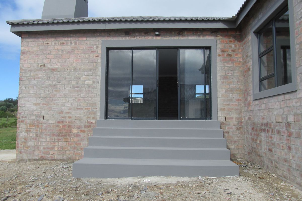 Rear exterior view of a brick house featuring a grey painted concrete staircase leading to sliding glass doors and a chimney stack.