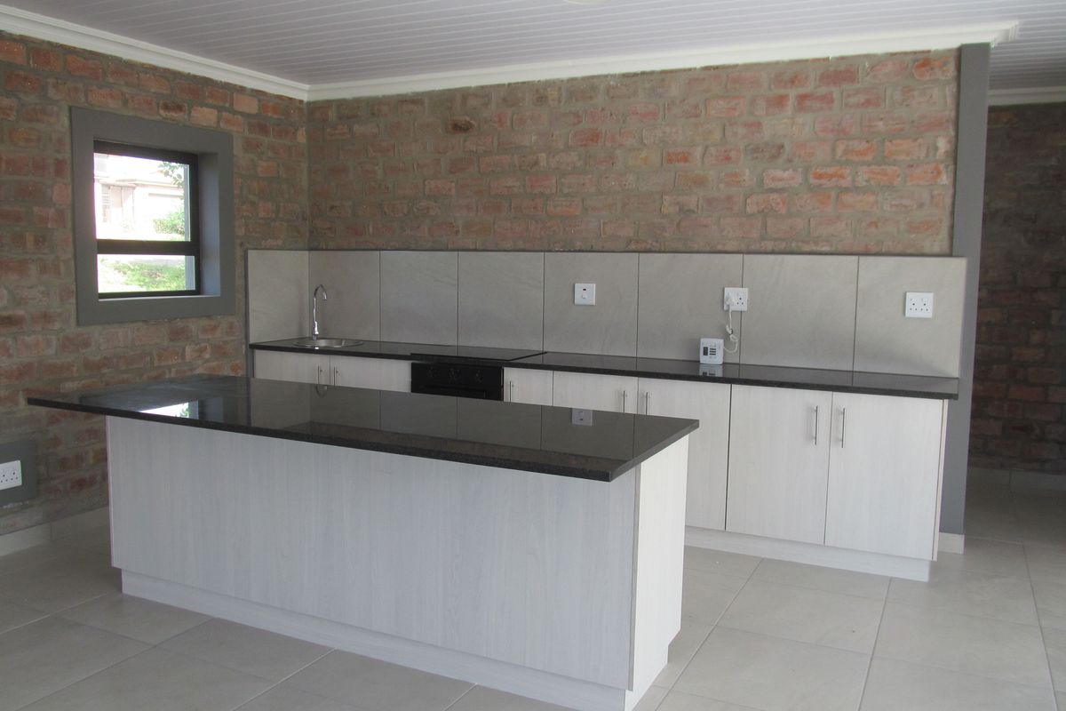 Modern kitchen featuring a central island with granite countertops, light-toned cabinetry, tiled splashback, and exposed brick feature walls.