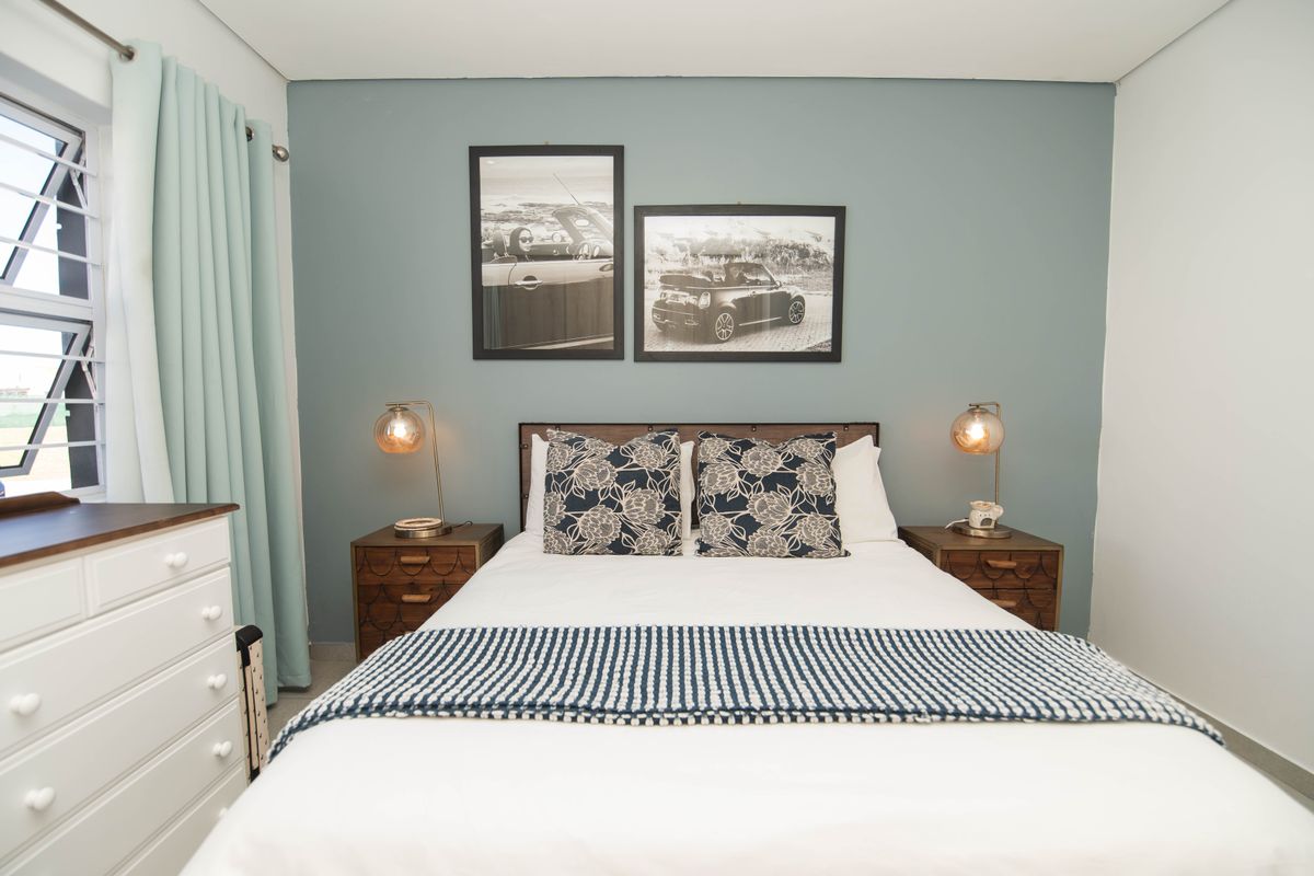A well-maintained bedroom featuring a soft blue accent wall, large window with natural light, and neutral flooring.