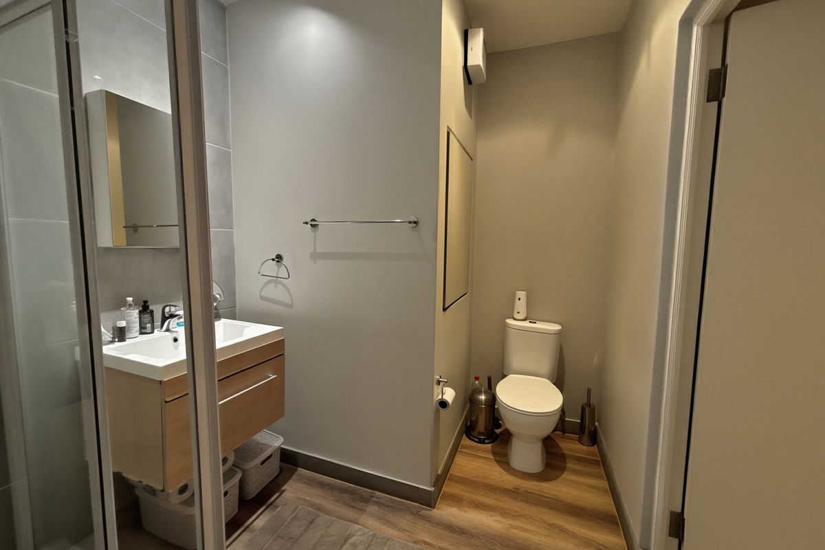 Modern bathroom featuring a vanity with integrated basin, a glass-enclosed shower, and a separate toilet area with wood-look flooring.