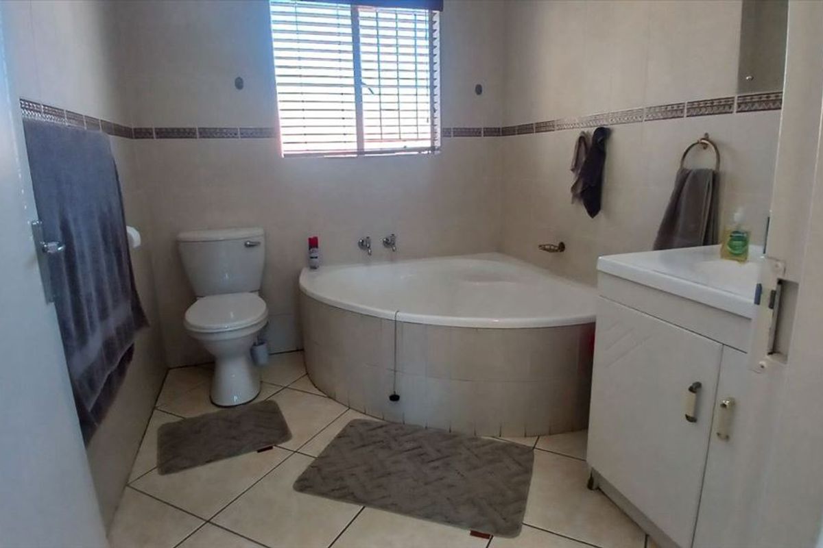 A functional bathroom featuring a corner bathtub, a standard toilet, and a vanity cabinet with a basin, finished with neutral wall and floor tiles.