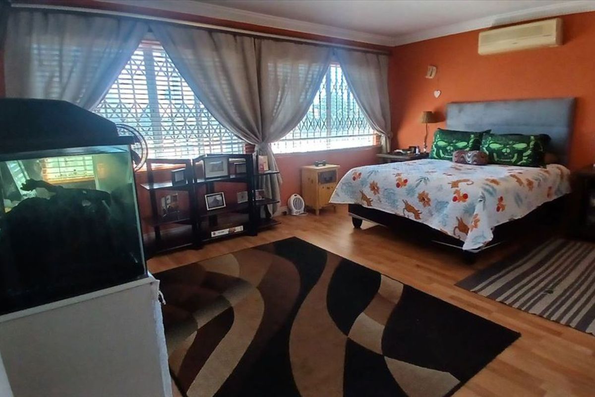 A spacious bedroom featuring laminate flooring, a wall-mounted air conditioning unit, and large windows with security bars.
