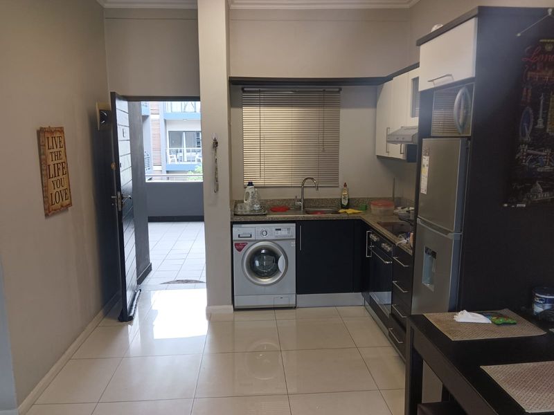 Compact kitchen area featuring built-in cabinetry, stone countertops, integrated sink, and under-counter laundry appliance, with direct access to an outdoor balcony.