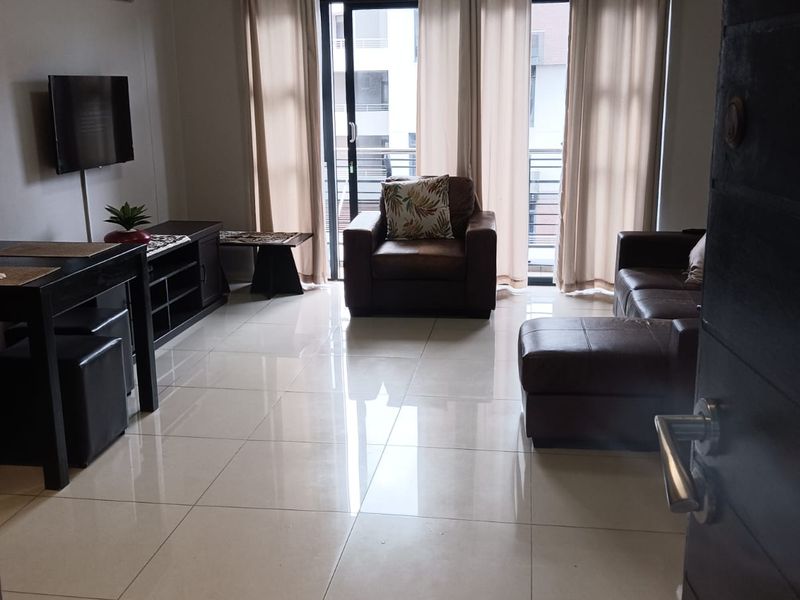 A well-maintained living room featuring large format floor tiles, neutral wall finishes, and sliding glass doors leading to a balcony.