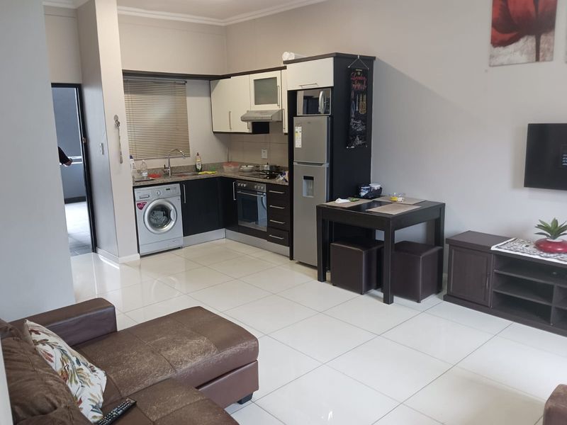 Open plan living area featuring a modern kitchen with built-in cabinetry, integrated oven, hob, extractor fan, and tiled flooring throughout.