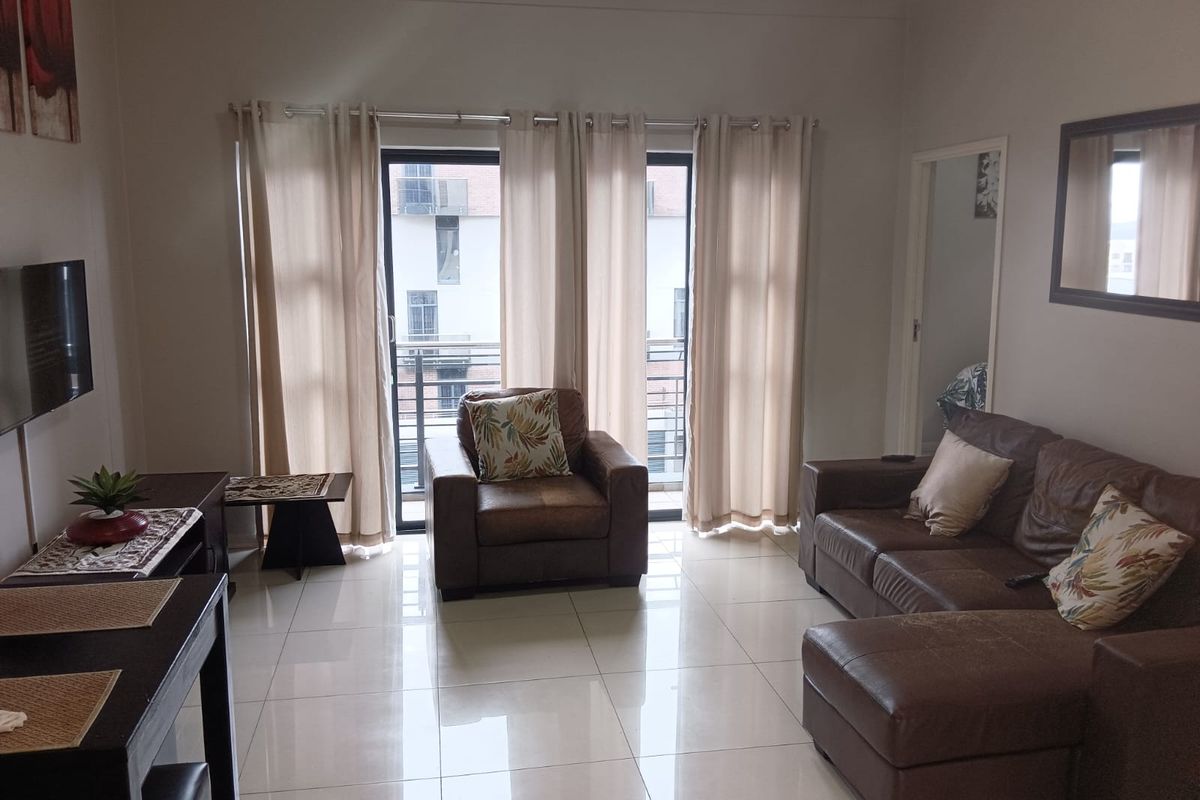 A well-lit living room featuring large sliding glass doors that open onto a balcony, complemented by neutral tiled flooring throughout.