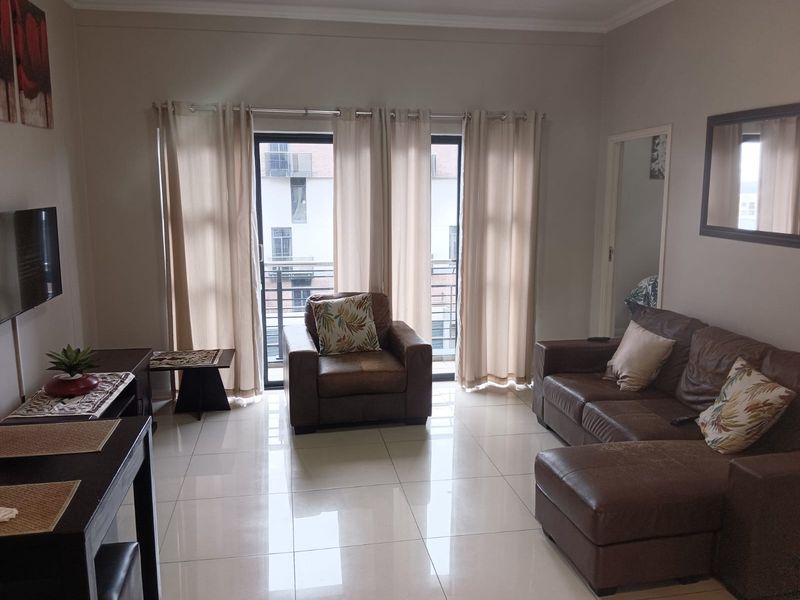A well-lit living room featuring large sliding glass doors that open onto a balcony, complemented by neutral tiled flooring throughout.