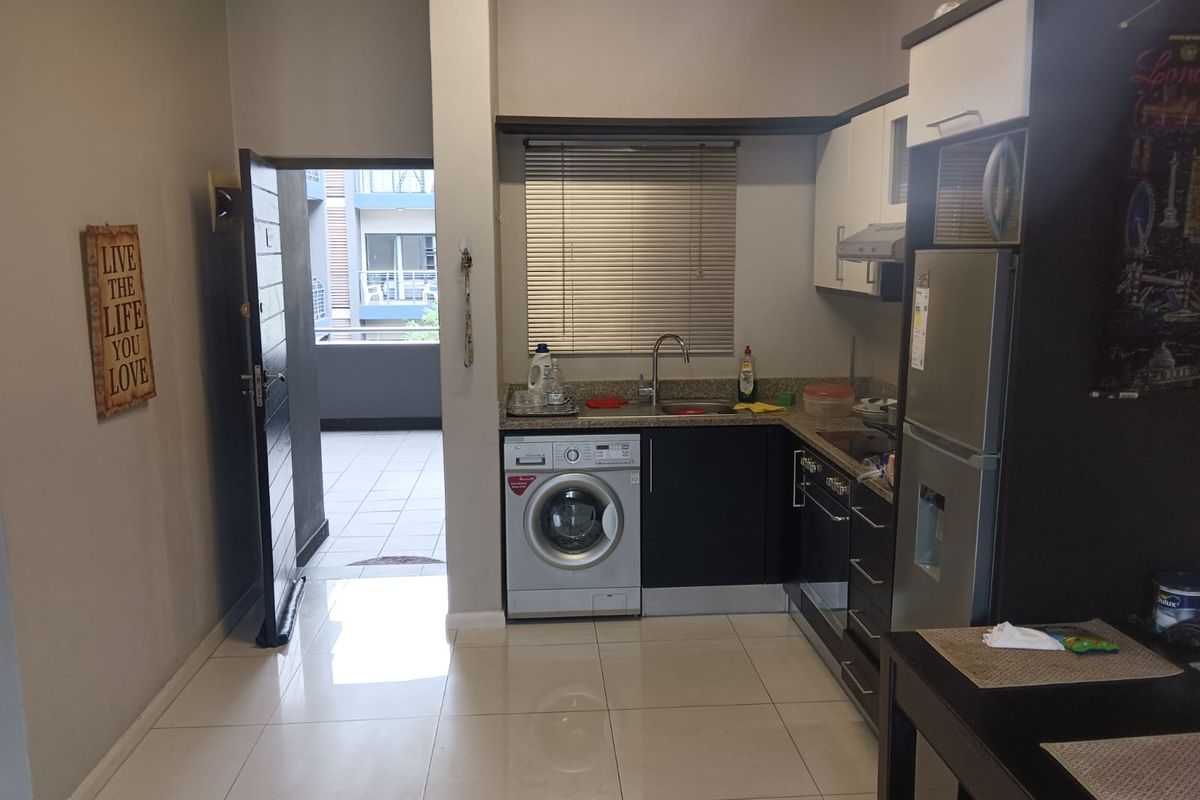 Compact kitchen area featuring built-in cabinetry, stone countertops, integrated sink, and under-counter laundry appliance, with direct access to an outdoor balcony.