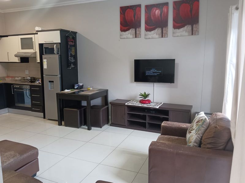Open-plan living area featuring a modern kitchen with built-in cabinetry, oven, and hob, seamlessly flowing into a comfortable lounge space with tiled flooring.