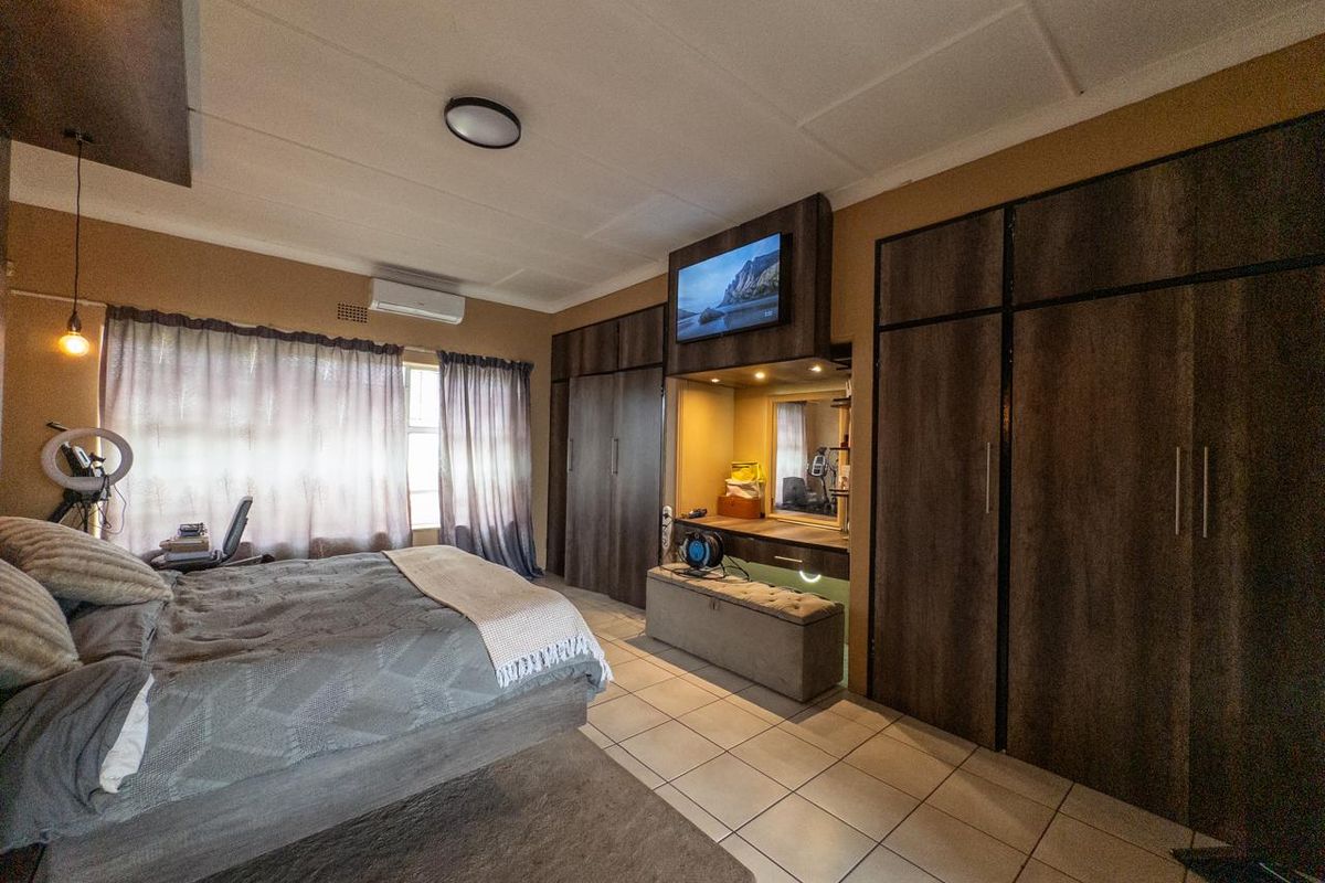 A spacious bedroom featuring extensive built-in cabinetry, a dedicated vanity area, tiled flooring, and a wall-mounted air conditioning unit.