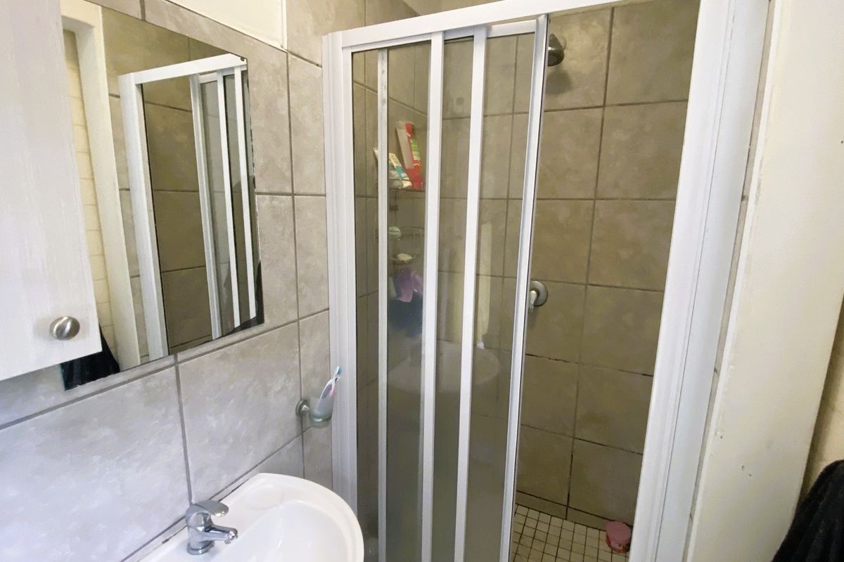 A compact bathroom featuring a tiled shower enclosure with a sliding door, a wall-mounted mirror, and a pedestal basin.