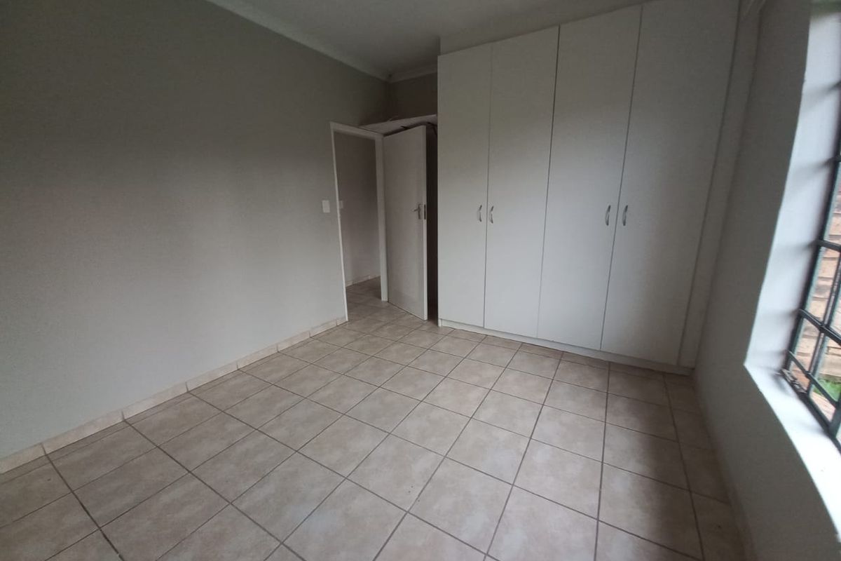 A bright, empty bedroom featuring neutral tiled flooring, built-in white cabinetry, and a large window allowing for natural light.